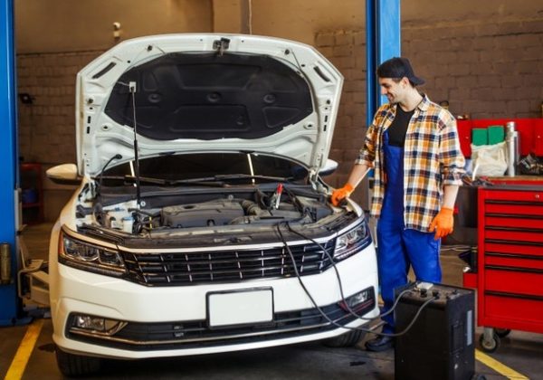 full-length-shot-handsome-auto-mechanic-charging-battery-using-wire-cables-modern-service-station_496169-1021